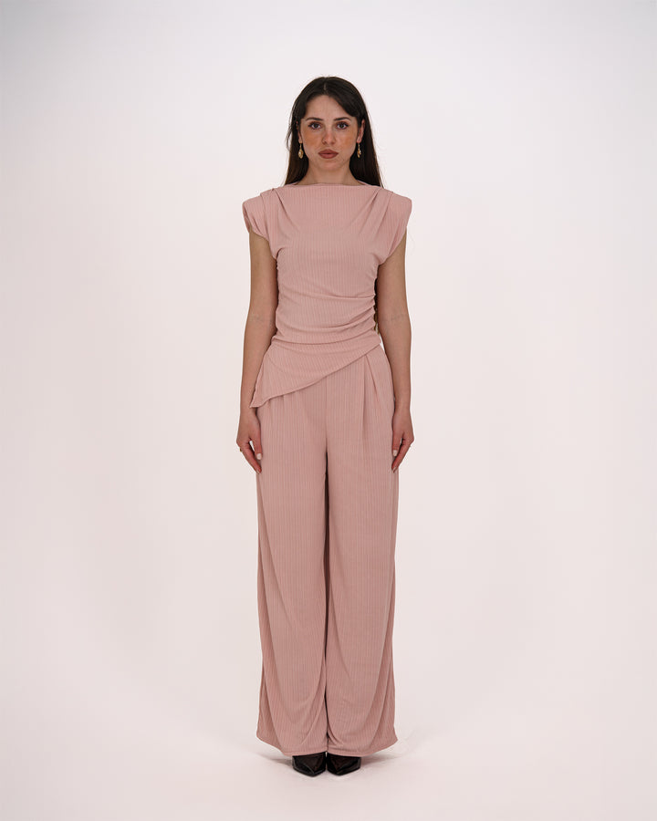 Dieser Einteiler in zartem Roséton überzeugt mit seinem femininen Schnitt und eleganten Drapierungen. Das Oberteil besticht durch raffinierte Faltenlegung und leicht überschnittene Schultern, während die weit geschnittene Hose fließend fällt und eine schmeichelhafte Silhouette zaubert. Ideal für besondere Anlässe, Business-Events oder festliche Abende. Der weich fließende Stoff sorgt für hohen Tragekomfort bei gleichzeitig stilvollem Auftritt.	•	Einteiler in elegantem Rosé
	•	Raffinierte Drapierung im Taill